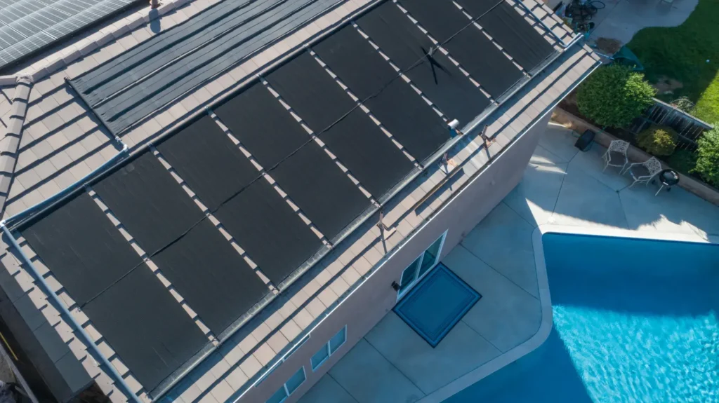 Solar pool heating panels installed on a residential roof beside a backyard swimming pool