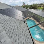 Solar pool heating panels installed on a shingle roof above a backyard pool