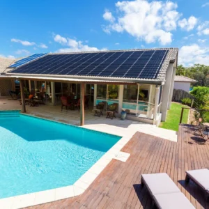 Residential swimming pool with rooftop solar panels on a backyard patio structure
