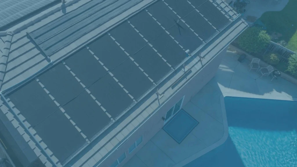 Solar pool heating panels installed on a residential roof beside a pool