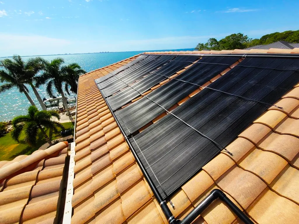 Solar pool heating panels on a tile roof near the water