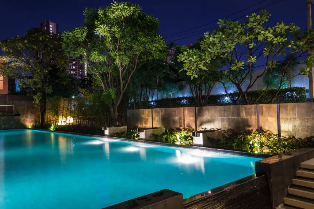Backyard pool illuminated with nightscape landscape lighting.